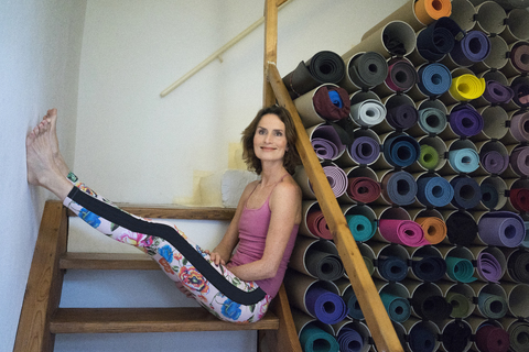 Entspannte reife Frau auf einer Treppe neben einem Sortiment von Yogamatten, lizenzfreies Stockfoto