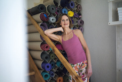Portrait of smiling mature woman standing next to assortment of yoga mats - MOEF00757