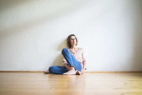 Reife Frau sitzt auf dem Boden in einem leeren Raum und denkt nach - MOEF00760