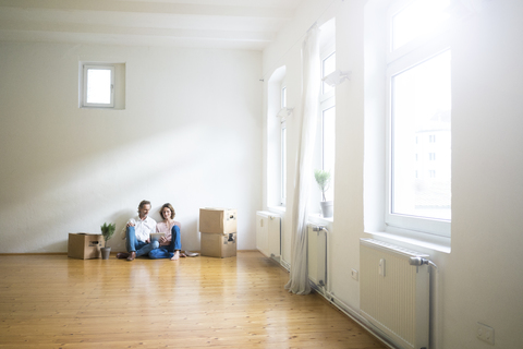 Mature couple sitting on floor in empty room next to cardboard boxes using tablet stock photo