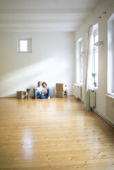 Mature couple sitting on floor in empty room next to cardboard boxes using tablet - MOEF00763