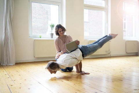 Ältere Frau benutzt Tablet auf dem Rücken eines Mannes, der einen Handstand macht, lizenzfreies Stockfoto