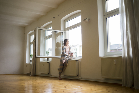 Reife Frau in leerem Raum hält Tablet Blick aus dem Fenster, lizenzfreies Stockfoto