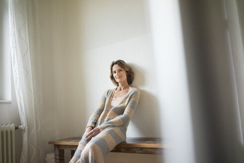 Portrait of smiling mature woman sitting on wooden bench at home - MOEF00783