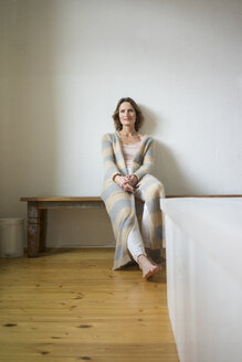 Portrait of smiling mature woman sitting on wooden bench at home - MOEF00784