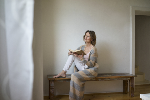 Mature woman sitting on wooden bench at home reading book stock photo