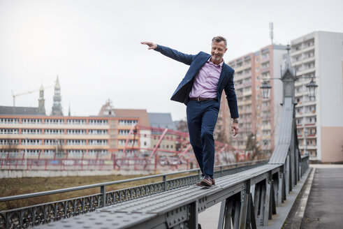 Stilvoller reifer Geschäftsmann im blauen Anzug balanciert auf dem Geländer einer Brücke - DIGF03279