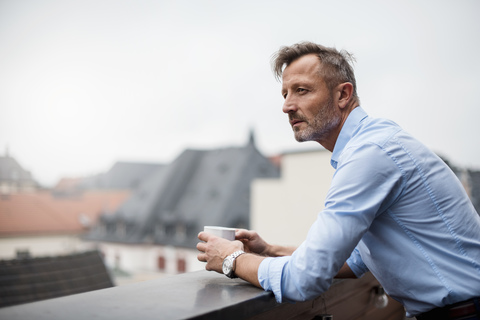 Portrait of mature businessman with cup of coffee on roof terrace stock photo