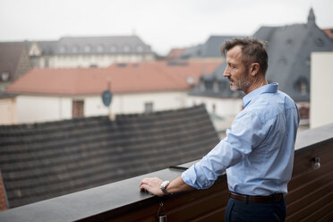 Mature businessman standing on roof terrace looking at view - DIGF03282