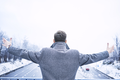 Back view of man with arms outstretched standing on bridge above motorway stock photo