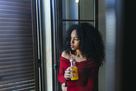 Young woman with beverage looking out of window stock photo