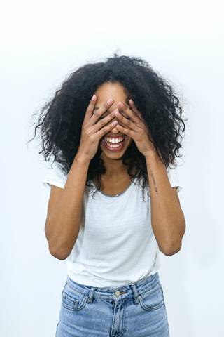 Porträt einer lachenden jungen Frau, die ihre Augen mit den Händen bedeckt, lizenzfreies Stockfoto