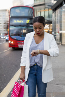 UK, London, Frau mit Einkaufstüten in der Stadt, die die Zeit überprüft - MAUF01340