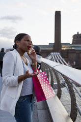 UK, London, genervte Frau mit Einkaufstüten am Handy in der Stadt - MAUF01348