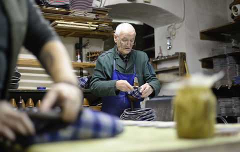 Älterer Schuhmacher bei der Arbeit an Hausschuhen in der Werkstatt, lizenzfreies Stockfoto