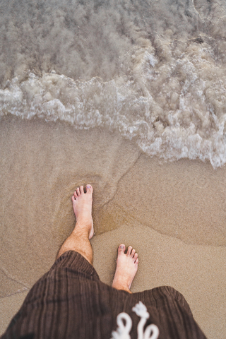 Thailand, Füße eines am Strand stehenden Mannes am Meer, lizenzfreies Stockfoto