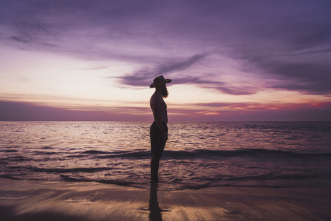 Thailand, Phuket, Silhouette eines Mannes mit Hut, der bei Sonnenuntergang am Meer steht, lizenzfreies Stockfoto