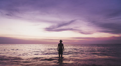 Thailand, Phuket, silhouette of man wearing hat wading at seafront by sunset stock photo