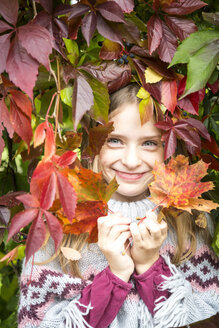 Porträt eines glücklichen Mädchens, das sich hinter Herbstblättern versteckt - SARF03554