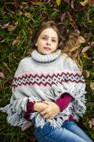 Portrait of girl wearing poncho lying on autumnal meadow stock photo