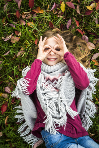 Portrait of smiling girl lying on autumnal meadow looking through her fingers formed like spectacles stock photo