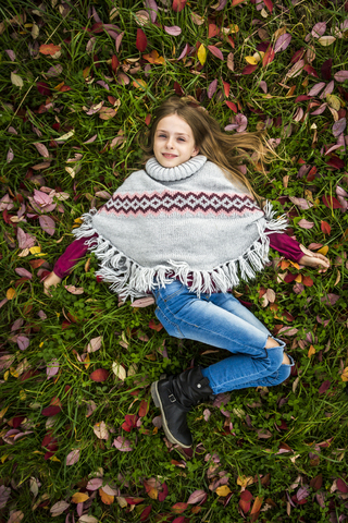 Porträt eines lächelnden Mädchens mit Poncho auf einer herbstlichen Wiese liegend, lizenzfreies Stockfoto