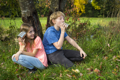 Boy and girl on a meadow having fun with tin can phone stock photo