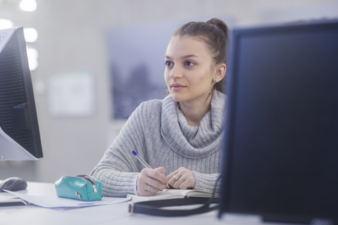 Porträt einer jungen Frau bei der Arbeit am Schreibtisch in einem Büro, lizenzfreies Stockfoto