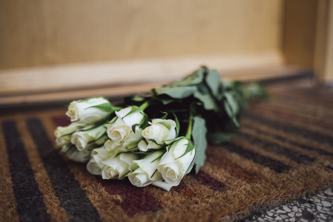 Ein Strauß weißer Abschiedsblumen liegt auf der Fußmatte vor der Wohnungstür des verstorbenen Nachbarn, lizenzfreies Stockfoto