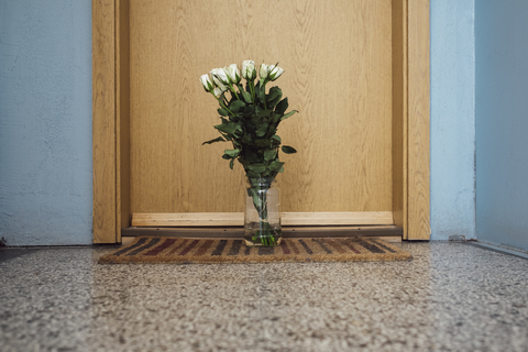 Vase mit Abschiedsblumen auf der Fußmatte vor der Wohnungstür des verstorbenen Nachbarn, lizenzfreies Stockfoto