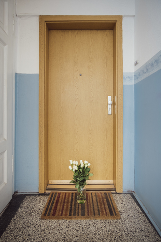 Vase with bunch of white farewell flowers on floor mat at apartment door of deceased neighbour stock photo