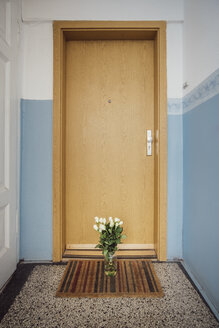 Vase with bunch of white farewell flowers on floor mat at apartment door of deceased neighbour - JSCF00060