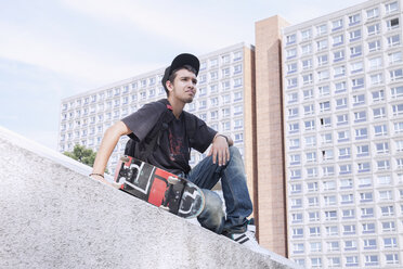 Thoughtful young man with skateboard sitting against building - FSIF00019