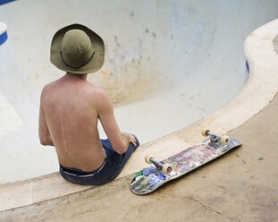 Rückansicht eines Mannes mit Skateboard, der auf dem Rand einer Skateboarding-Schüssel sitzt - FSIF00022