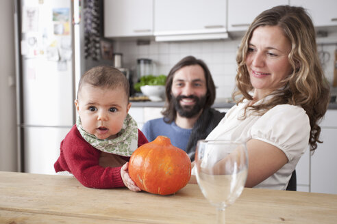Eltern mit einem kleinen Mädchen, das einen Kürbis am Tisch in der Küche hält - FSIF00034