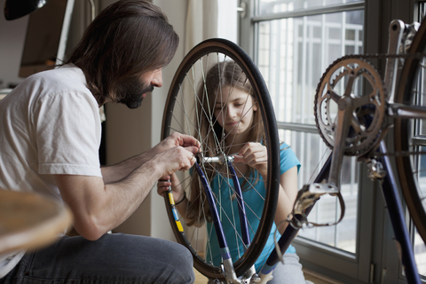 Vater und Tochter reparieren gemeinsam zu Hause ein Fahrrad, lizenzfreies Stockfoto