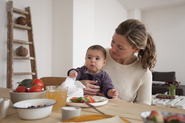 Mother looking at baby girl while sitting at table in house - FSIF00042