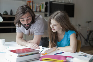 Vater hilft Tochter bei den Hausaufgaben am Tisch - FSIF00046