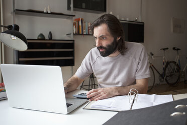 Mittlerer erwachsener Mann arbeitet zu Hause am Laptop - FSIF00051