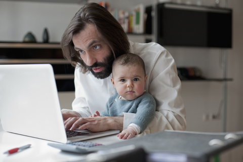 Mann arbeitet am Laptop, während er mit seinem kleinen Mädchen zu Hause sitzt, lizenzfreies Stockfoto