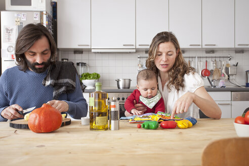 Vater schneidet Gemüse mit Mutter spielt mit Baby Mädchen in der Küche - FSIF00068