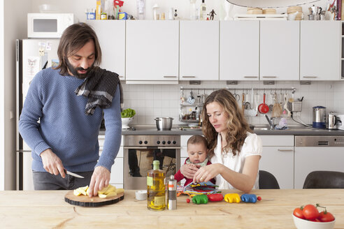 Vater hackt Gemüse, während Mutter und kleines Mädchen in der Küche spielen - FSIF00070