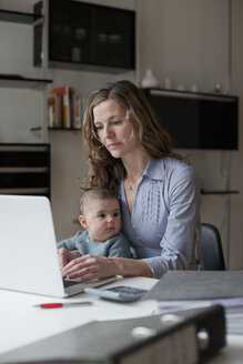 Frau benutzt Laptop, während sie mit ihrem kleinen Mädchen zu Hause sitzt - FSIF00083