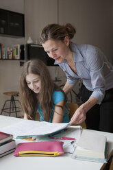 Mother helping daughter in doing homework at table - FSIF00098