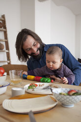 Happy father with baby girl playing at table - FSIF00100