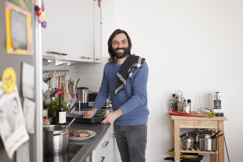Lächelnder Mann, der wegschaut, während er in der heimischen Küche Essen zubereitet, lizenzfreies Stockfoto