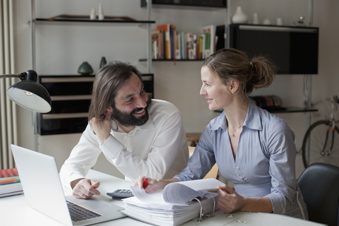 Mid adult couple looking at each other while working at home, lizenzfreies Stockfoto