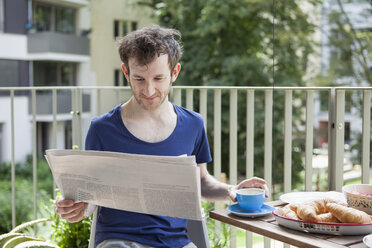 Junger Mann liest Zeitung beim Frühstück auf der Veranda - FSIF00191