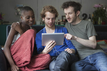 Freunde benutzen gemeinsam ein digitales Tablet auf dem Sofa zu Hause - FSIF00192