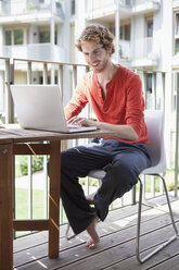 Lächelnder Mann mit Laptop auf Veranda - FSIF00195